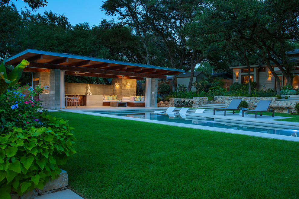 Photo of a large modern backyard rectangular lap pool in Austin with a pool house and natural stone pavers.