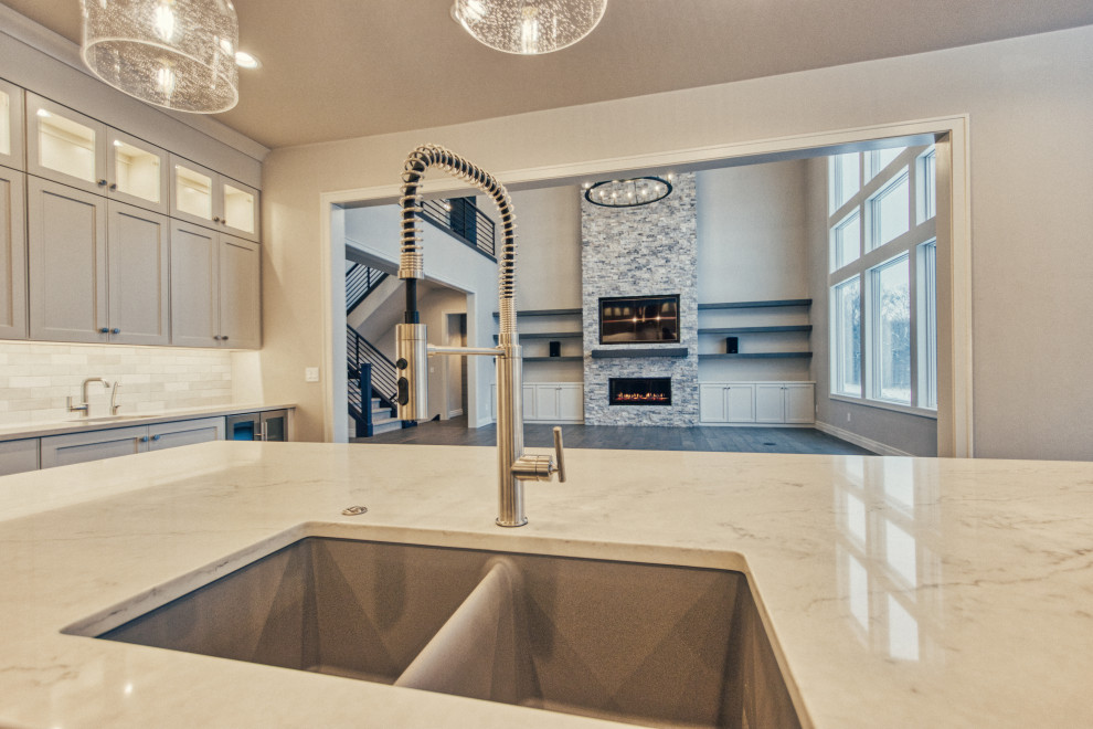Inspiration for a large transitional l-shaped medium tone wood floor and brown floor kitchen pantry remodel with an undermount sink, shaker cabinets, white cabinets, quartz countertops, white backsplash, ceramic backsplash, stainless steel appliances, an island and white countertops