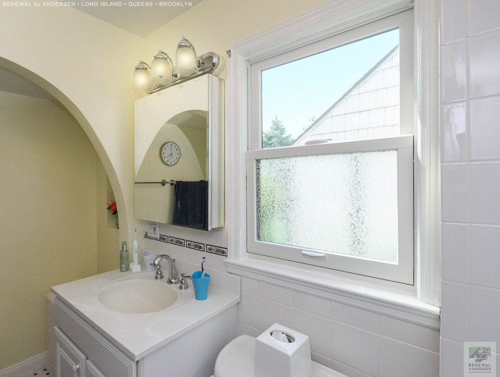 Example of a mid-sized white tile and ceramic tile ceramic tile, multicolored floor, single-sink and vaulted ceiling bathroom design in New York with white cabinets, a two-piece toilet, yellow walls, an integrated sink, white countertops and a built-in vanity