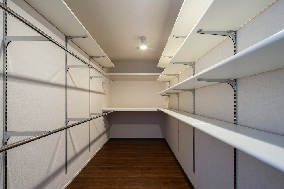 Diseño de armario vestidor unisex minimalista grande con armarios abiertos, puertas de armario blancas, suelo de madera oscura, suelo marrón y papel pintado