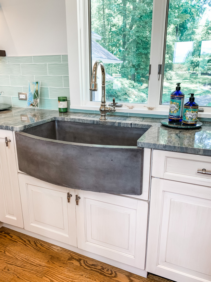 Mid-sized transitional u-shaped open plan kitchen in Baltimore with a farmhouse sink, raised-panel cabinets, white cabinets, granite benchtops, blue splashback, glass tile splashback, panelled appliances, medium hardwood floors, no island, brown floor, multi-coloured benchtop and vaulted.