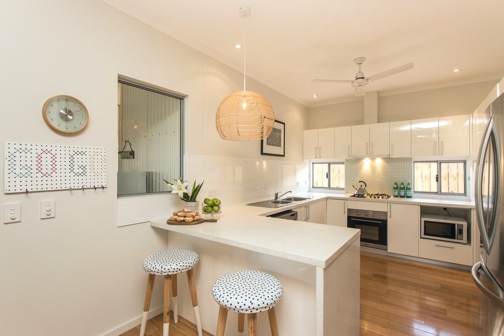 Photo of a small contemporary u-shaped separate kitchen in Dunedin with a double-bowl sink, flat-panel cabinets, white cabinets, quartz benchtops, green splashback, mosaic tile splashback, stainless steel appliances and bamboo floors.
