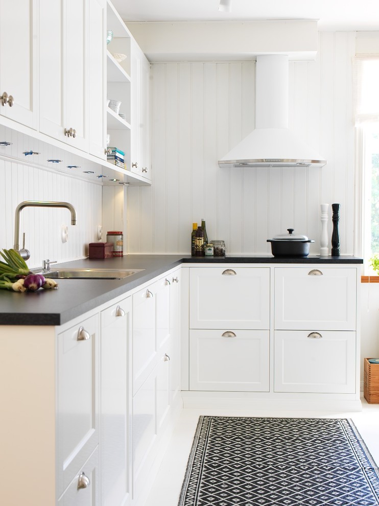 Photo of a mid-sized country l-shaped kitchen in Malmo with a drop-in sink, shaker cabinets, white cabinets, white splashback and painted wood floors.