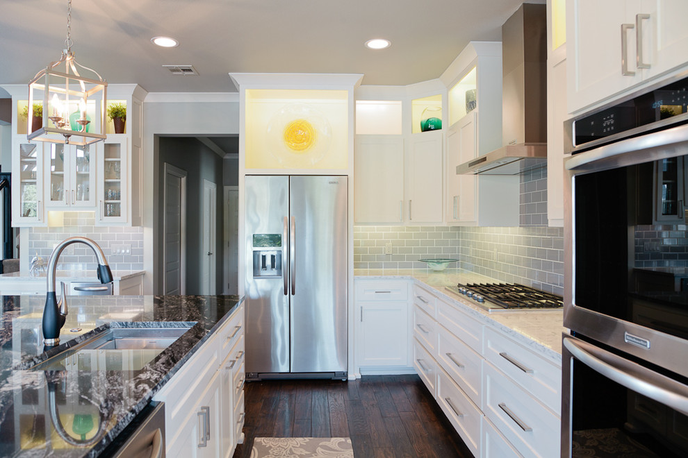 Inspiration for a mid-sized coastal u-shaped dark wood floor eat-in kitchen remodel with an undermount sink, shaker cabinets, white cabinets, granite countertops, gray backsplash, glass tile backsplash, stainless steel appliances and an island