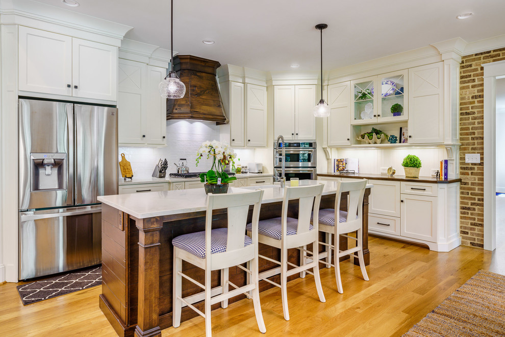 Large transitional u-shaped medium tone wood floor and brown floor eat-in kitchen photo with a farmhouse sink, recessed-panel cabinets, white cabinets, quartz countertops, white backsplash, ceramic backsplash, stainless steel appliances, an island and white countertops