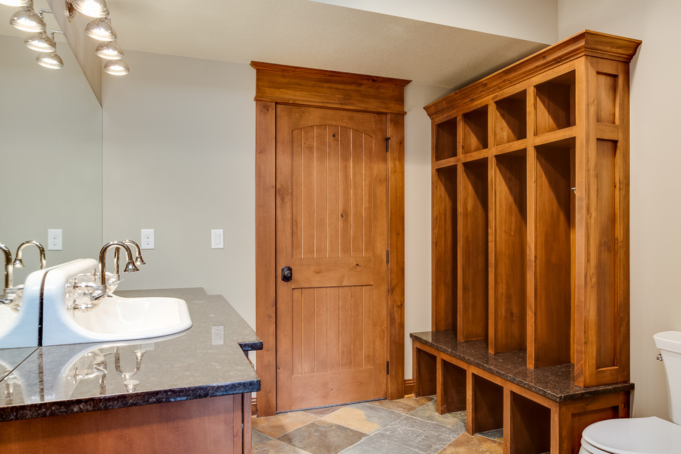 Example of a large mountain style multicolored tile and stone tile slate floor doorless shower design with a console sink, flat-panel cabinets, medium tone wood cabinets, granite countertops, a two-piece toilet and beige walls