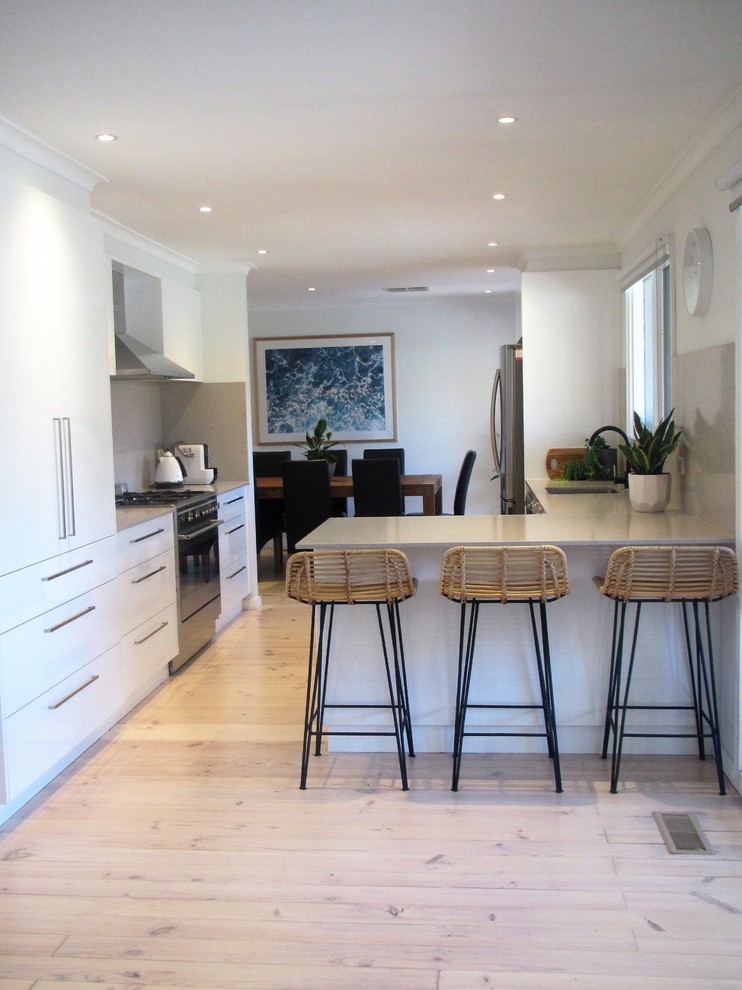 This is an example of a contemporary kitchen in Melbourne with an undermount sink, white cabinets, granite benchtops, grey splashback, stone slab splashback, stainless steel appliances, light hardwood floors and white floor.
