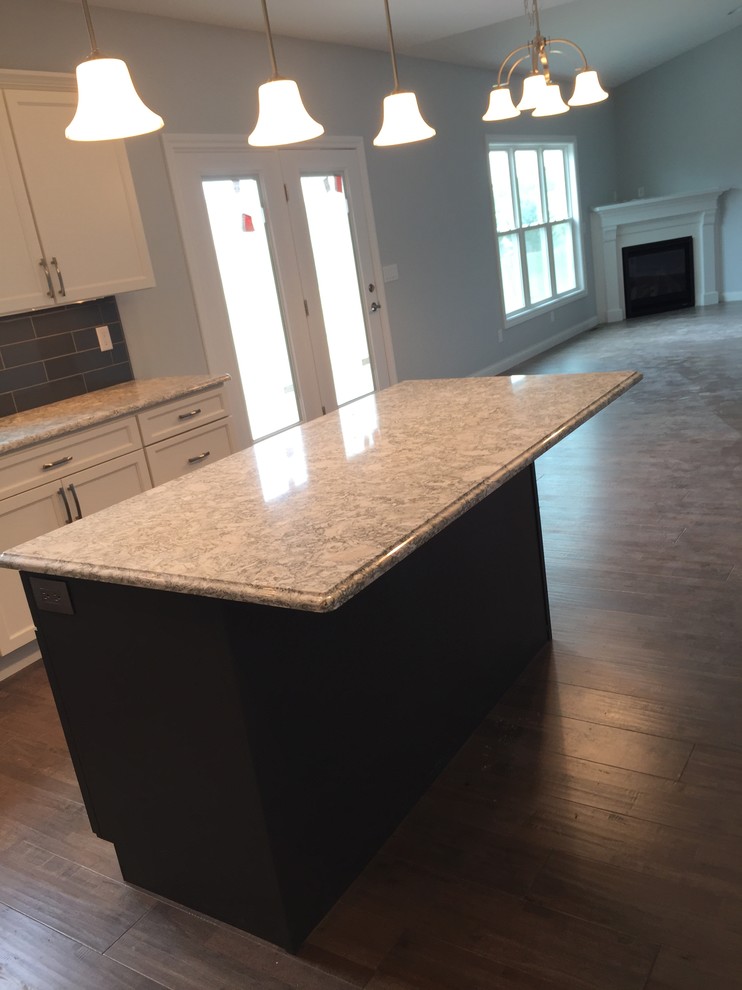 Example of a large transitional l-shaped open concept kitchen design with an undermount sink, raised-panel cabinets, white cabinets, quartz countertops, gray backsplash, stainless steel appliances and an island
