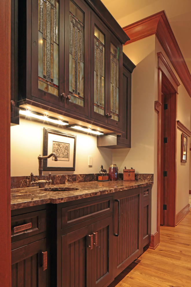 Small arts and crafts single-wall wet bar in DC Metro with an undermount sink, light hardwood floors, recessed-panel cabinets, dark wood cabinets and marble benchtops.