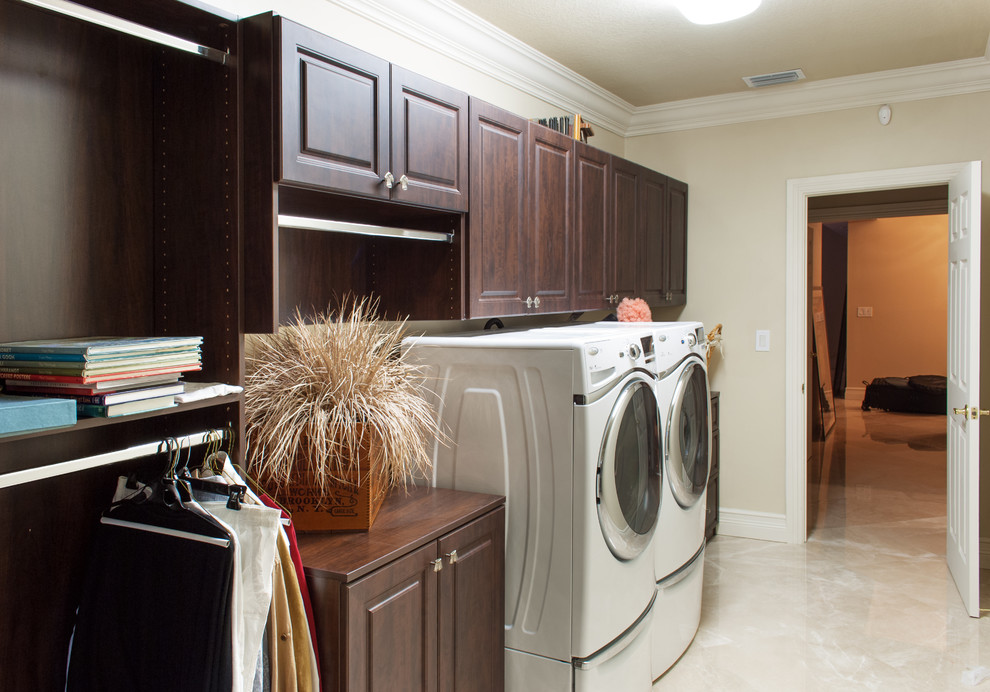 Design ideas for a mid-sized traditional single-wall utility room in Miami with raised-panel cabinets, dark wood cabinets, wood benchtops, beige walls, marble floors and a side-by-side washer and dryer.