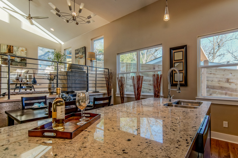 Inspiration for a small modern single-wall home design remodel in Austin with a double-bowl sink, flat-panel cabinets, dark wood cabinets, granite countertops, white backsplash, glass tile backsplash, stainless steel appliances, beige walls, engineered wood floors and an island