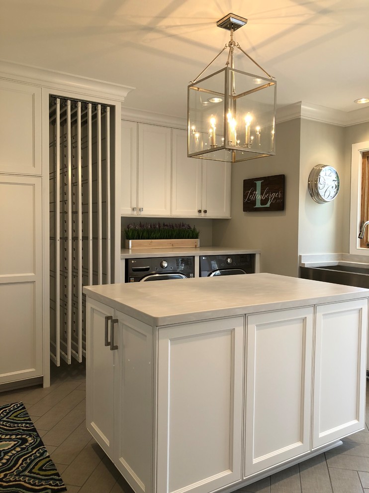 Design ideas for a mid-sized transitional galley utility room in Milwaukee with a farmhouse sink, recessed-panel cabinets, white cabinets, grey walls, ceramic floors, a concealed washer and dryer, brown floor and grey benchtop.