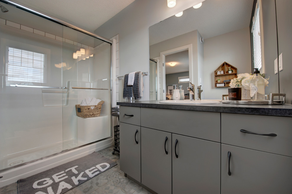 Mid-sized transitional master bathroom in Edmonton with flat-panel cabinets, grey cabinets, an alcove shower, a one-piece toilet, yellow tile, ceramic tile, grey walls, vinyl floors, a drop-in sink, laminate benchtops, grey floor, a sliding shower screen and black benchtops.