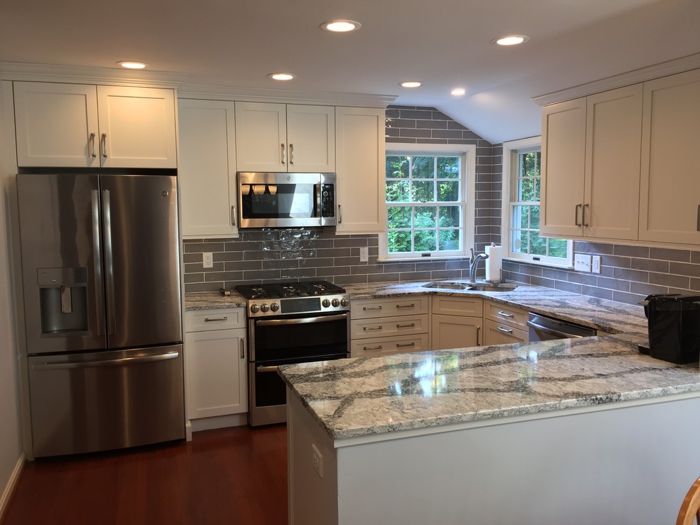 Inspiration for a mid-sized transitional u-shaped medium tone wood floor and red floor open concept kitchen remodel in Baltimore with a double-bowl sink, shaker cabinets, white cabinets, quartz countertops, gray backsplash, ceramic backsplash, stainless steel appliances, no island and gray countertops