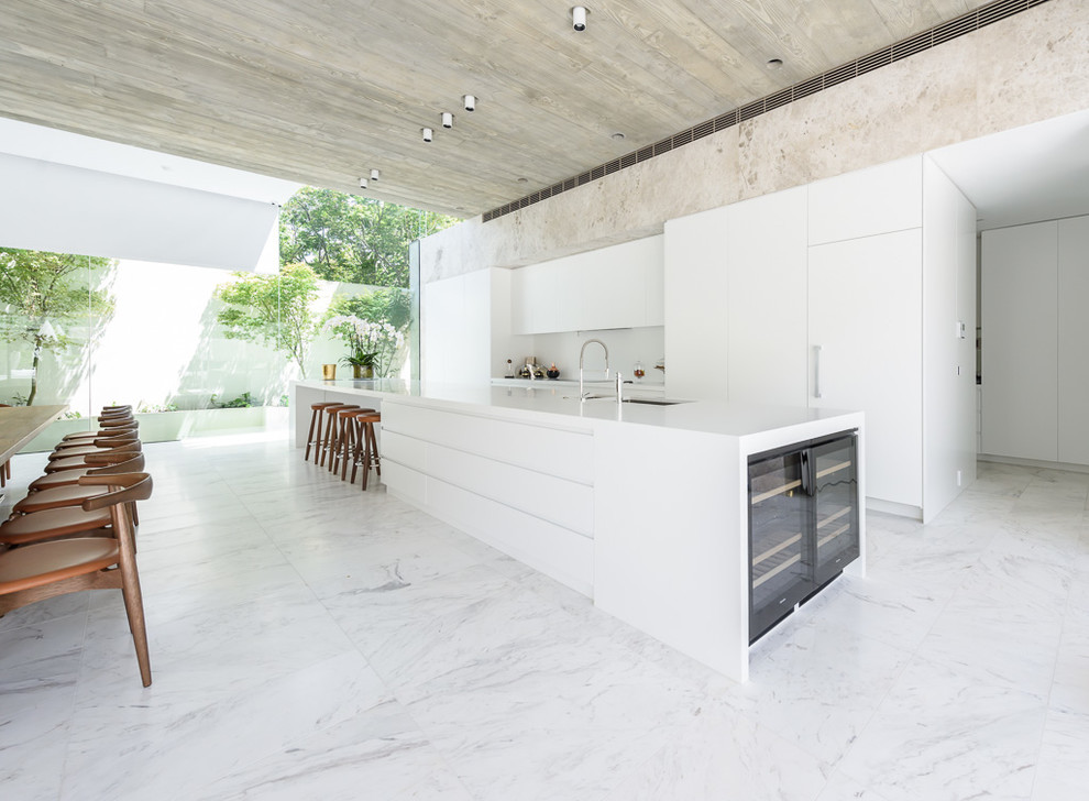 This is an example of an expansive contemporary galley open plan kitchen in Melbourne with flat-panel cabinets, white cabinets, solid surface benchtops, white splashback, panelled appliances, marble floors and with island.