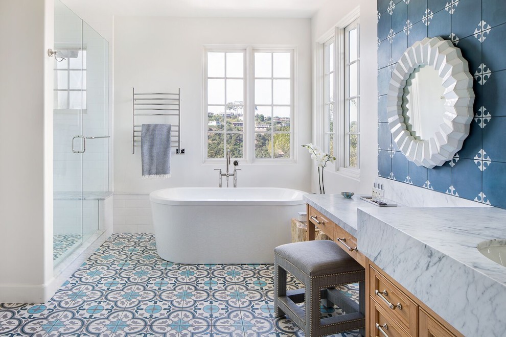 Photo of a mid-sized beach style master bathroom in Santa Barbara with a freestanding tub, an alcove shower, blue tile, cement tile, white walls, an undermount sink, marble benchtops, blue floor, a hinged shower door, grey benchtops, recessed-panel cabinets and medium wood cabinets.