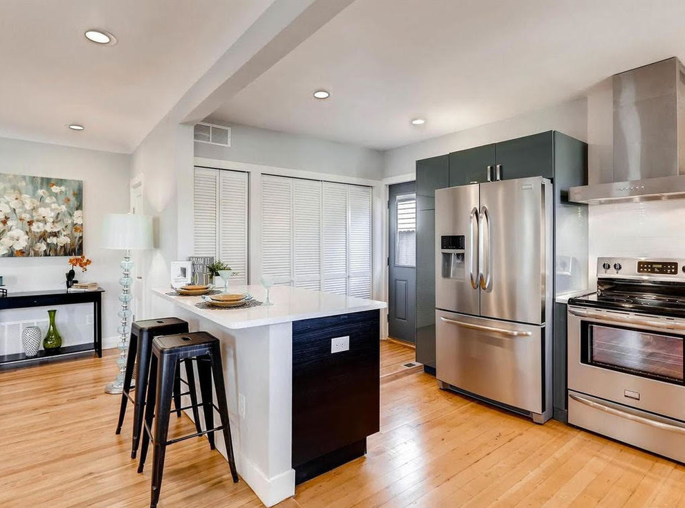 Mid-sized transitional single-wall light wood floor and brown floor enclosed kitchen photo with an undermount sink, recessed-panel cabinets, gray cabinets, quartz countertops, white backsplash, subway tile backsplash, stainless steel appliances and a peninsula