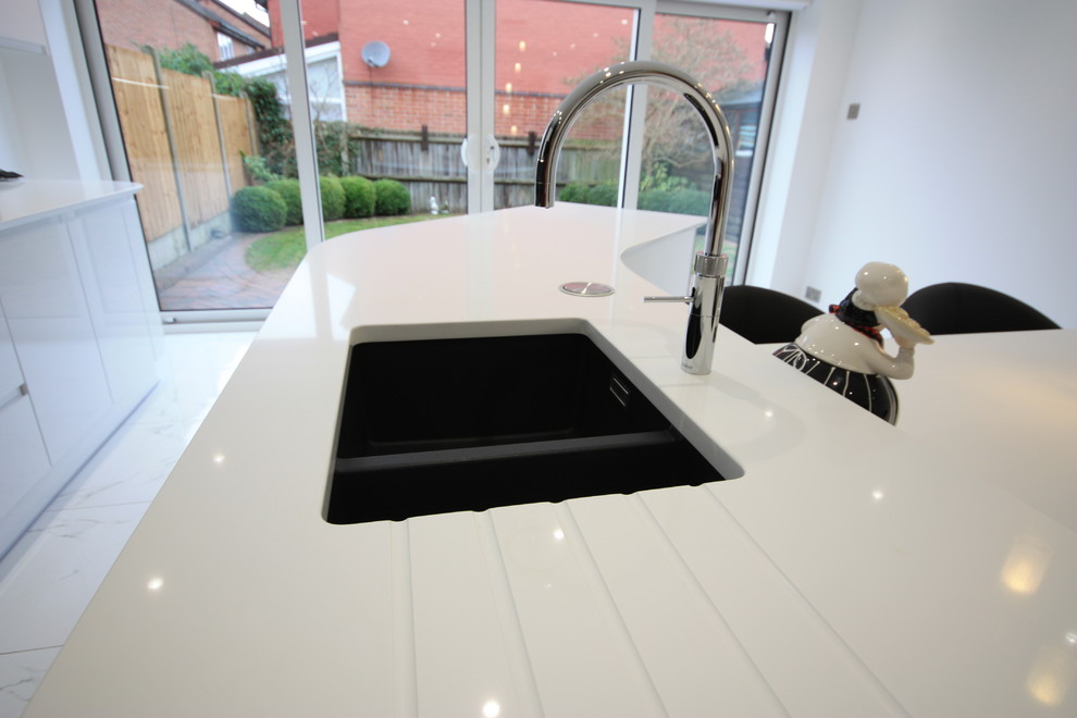 Photo of an expansive contemporary eat-in kitchen in Kent with a drop-in sink, flat-panel cabinets, white cabinets, quartzite benchtops, black splashback, glass sheet splashback, panelled appliances, porcelain floors, with island and white floor.