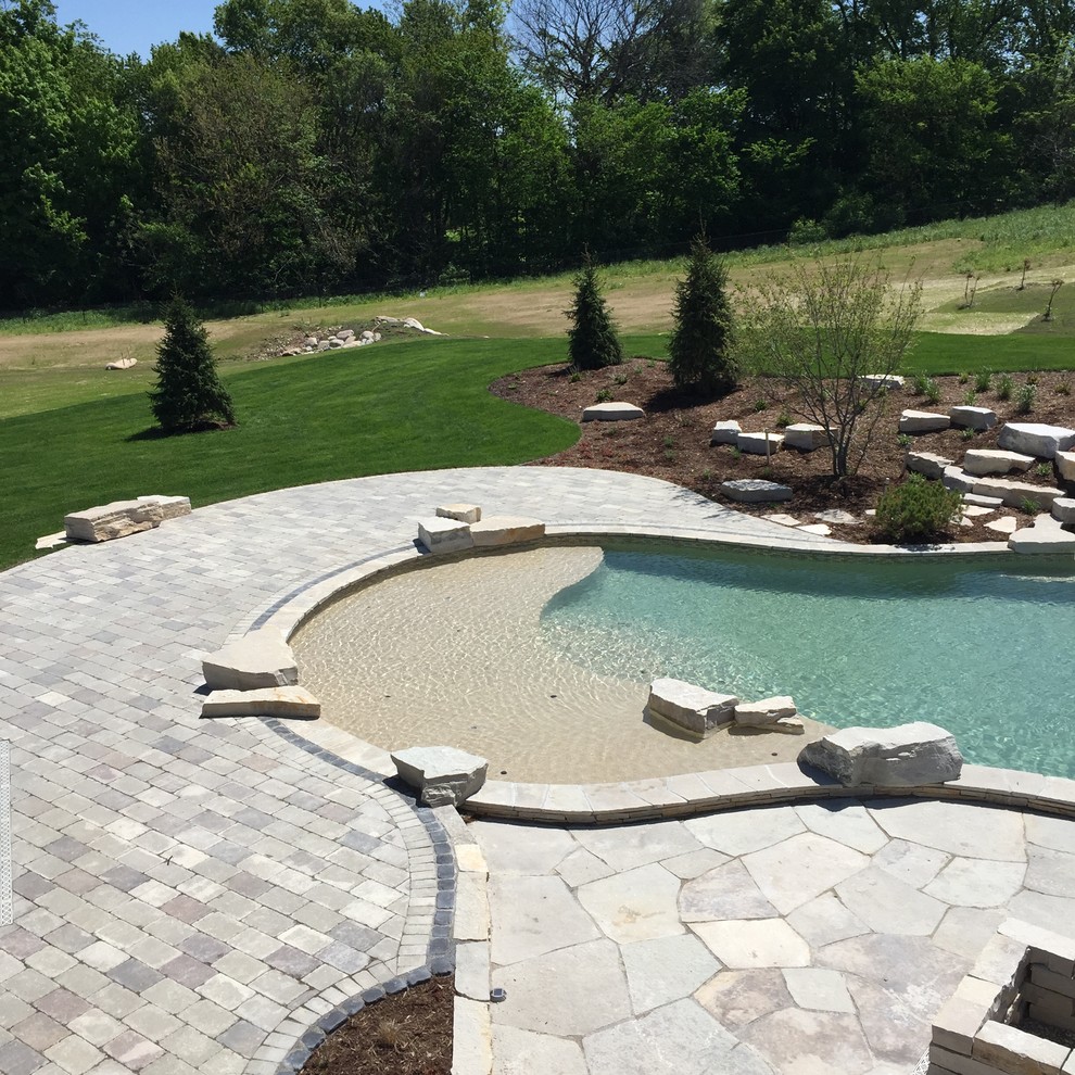 Expansive modern backyard custom-shaped natural pool in Grand Rapids with a water feature and natural stone pavers.