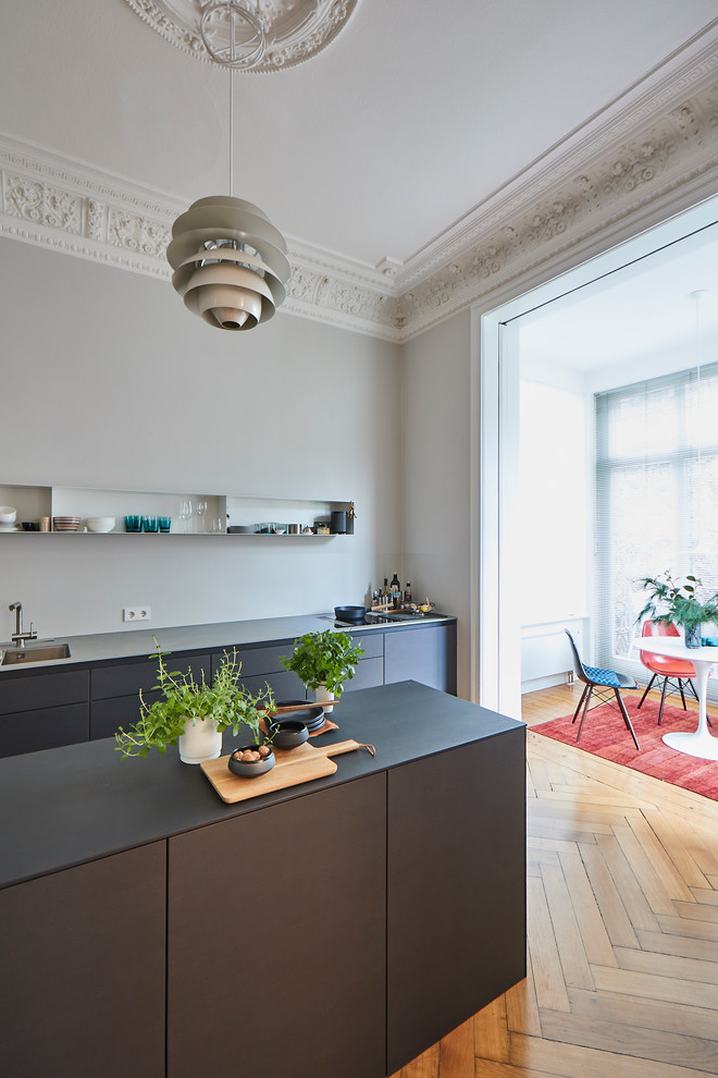 This is an example of a large modern single-wall open plan kitchen in Hamburg with a drop-in sink, flat-panel cabinets, grey cabinets, wood benchtops, grey splashback, painted wood floors, with island, brown floor and grey benchtop.