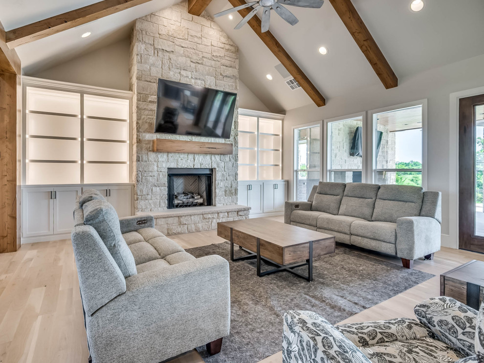 Inspiration for a large country open concept living room in Oklahoma City with beige walls, light hardwood floors, a stone fireplace surround, a wall-mounted tv and vaulted.