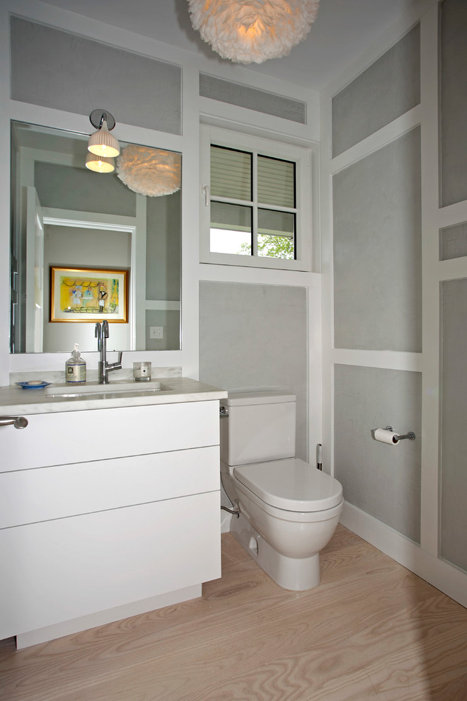 Inspiration for a mid-sized transitional 3/4 bathroom in New York with flat-panel cabinets, white cabinets, a one-piece toilet, grey walls, light hardwood floors, an undermount sink and marble benchtops.