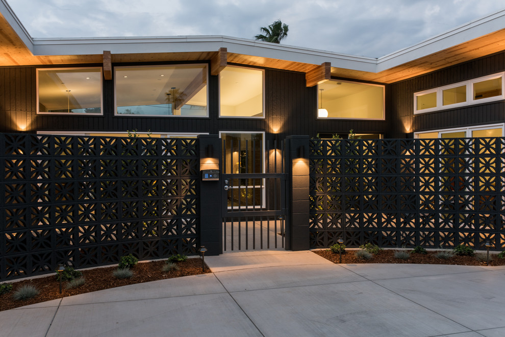 Mid-sized midcentury one-storey black house exterior in Other with wood siding.