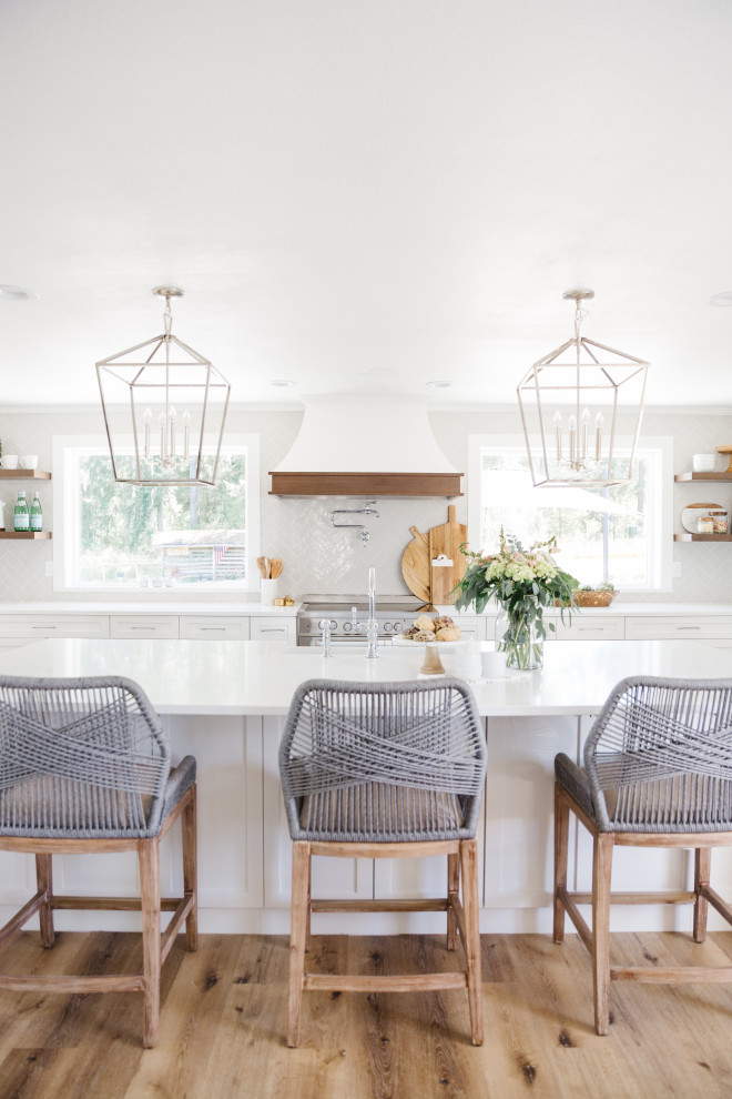 Large transitional u-shaped open plan kitchen in Seattle with a farmhouse sink, shaker cabinets, white cabinets, quartzite benchtops, white splashback, porcelain splashback, stainless steel appliances, light hardwood floors, with island, beige floor and white benchtop.