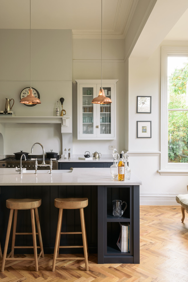This is an example of a large traditional l-shaped eat-in kitchen in Other with a farmhouse sink, shaker cabinets, blue cabinets, solid surface benchtops, white splashback, stainless steel appliances, medium hardwood floors, with island and brown floor.