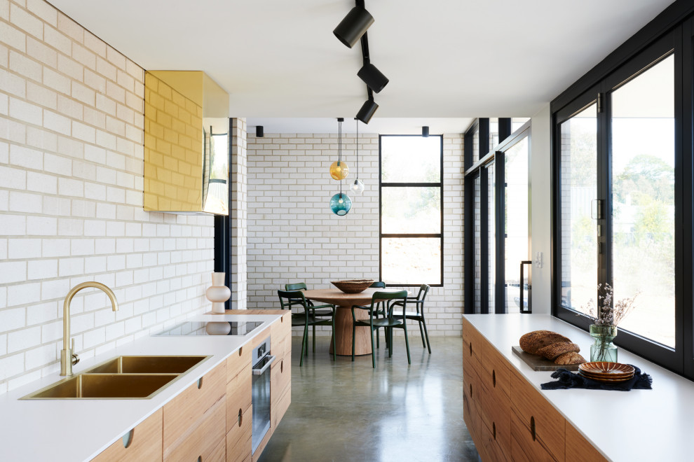 This is an example of a contemporary galley eat-in kitchen in Adelaide with a double-bowl sink, flat-panel cabinets, medium wood cabinets, quartz benchtops, white splashback, brick splashback, stainless steel appliances, concrete floors, no island, grey floor and white benchtop.