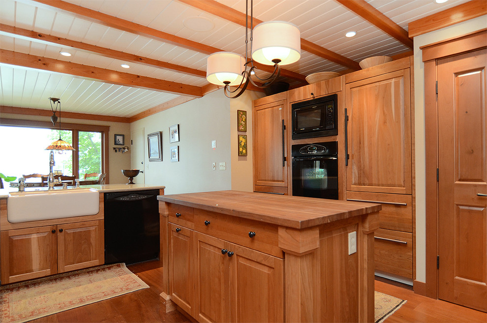Large arts and crafts u-shaped eat-in kitchen in Seattle with a farmhouse sink, raised-panel cabinets, medium wood cabinets, granite benchtops, black appliances, medium hardwood floors and with island.