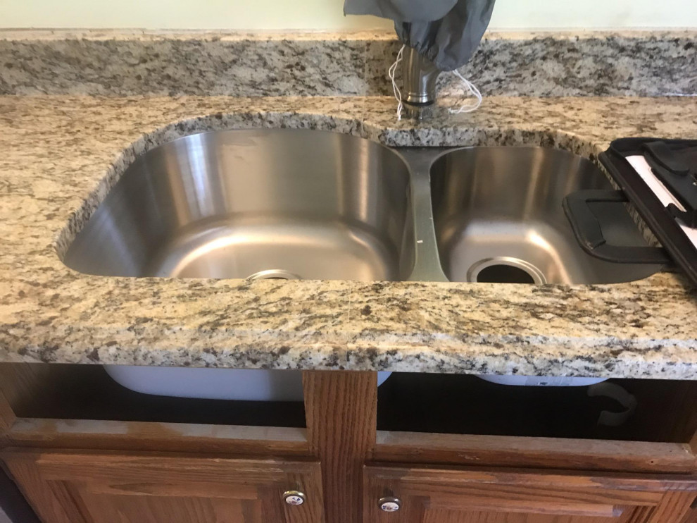 Small galley ceramic tile and brown floor enclosed kitchen photo with an undermount sink, recessed-panel cabinets, brown cabinets, granite countertops, stainless steel appliances, no island and brown countertops