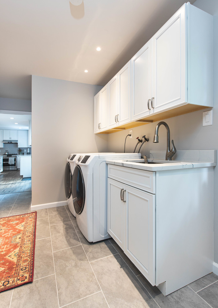 Large contemporary u-shaped laundry room in DC Metro with an undermount sink, raised-panel cabinets, white cabinets, quartz benchtops, grey splashback, subway tile splashback, vinyl floors, brown floor and white benchtop.