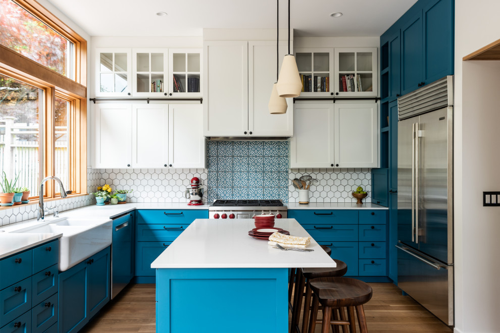 Photo of a large contemporary u-shaped kitchen in Seattle with a farmhouse sink, shaker cabinets, blue cabinets, quartz benchtops, white splashback, ceramic splashback, stainless steel appliances, with island, white benchtop, medium hardwood floors and brown floor.