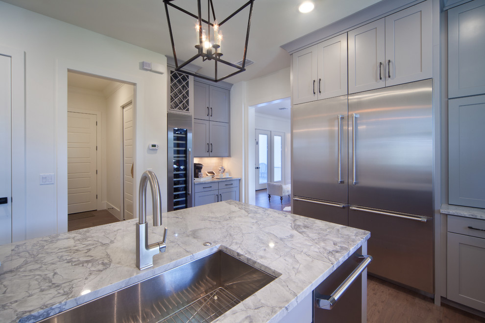 Inspiration for a mid-sized transitional l-shaped medium tone wood floor open concept kitchen remodel in Orlando with an undermount sink, recessed-panel cabinets, gray cabinets, granite countertops, white backsplash, ceramic backsplash, stainless steel appliances and an island