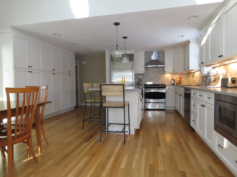 Inspiration for a large transitional l-shaped medium tone wood floor open concept kitchen remodel in Boston with an undermount sink, shaker cabinets, white cabinets, quartz countertops, gray backsplash, stainless steel appliances and an island