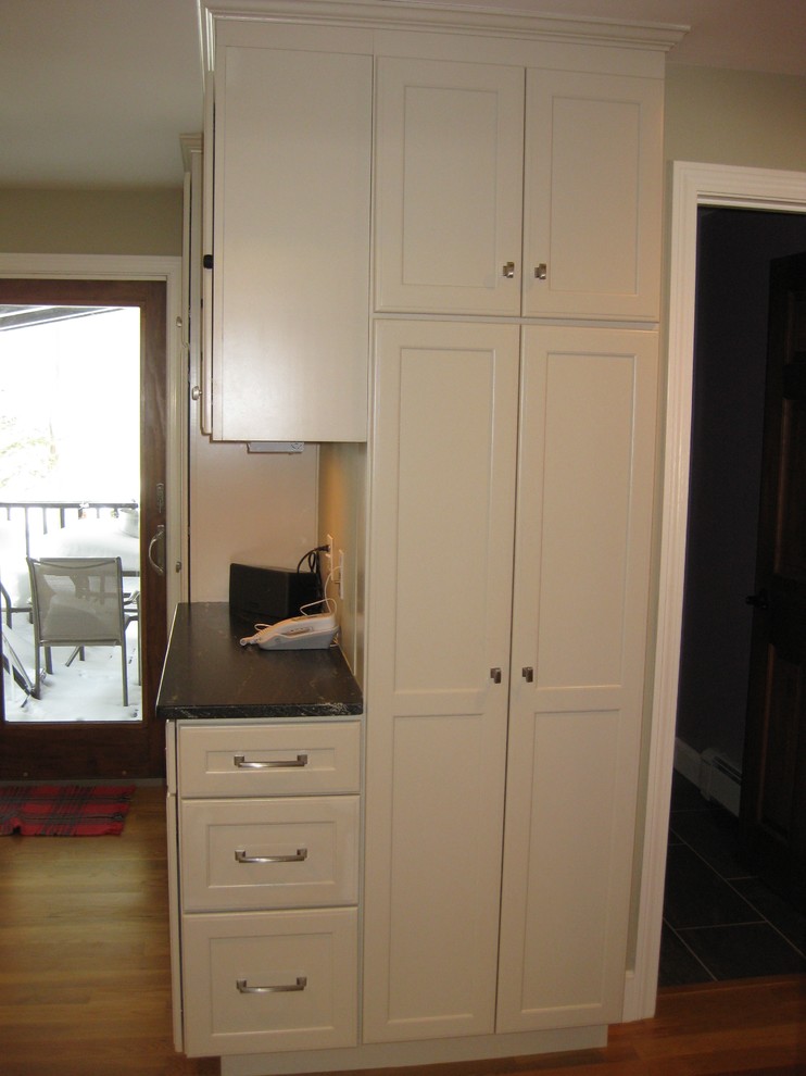 Inspiration for a transitional l-shaped medium tone wood floor eat-in kitchen remodel in Boston with an undermount sink, shaker cabinets, white cabinets, quartz countertops, white backsplash, ceramic backsplash, stainless steel appliances, an island and black countertops