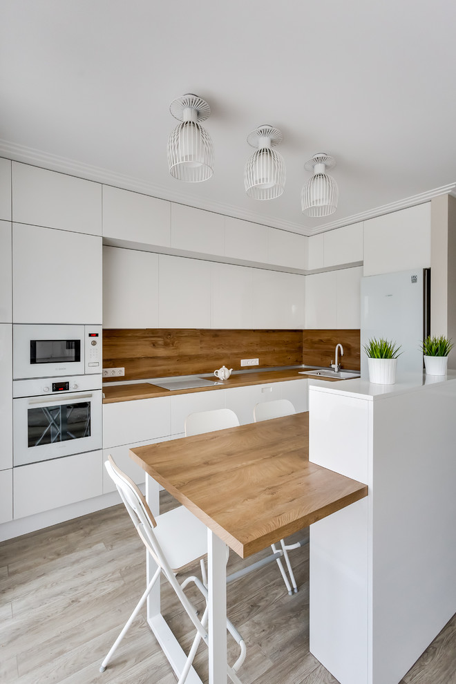Photo of a mid-sized contemporary l-shaped open plan kitchen in Other with a drop-in sink, flat-panel cabinets, white cabinets, white appliances, with island, brown splashback, brown benchtop, wood benchtops and porcelain splashback.