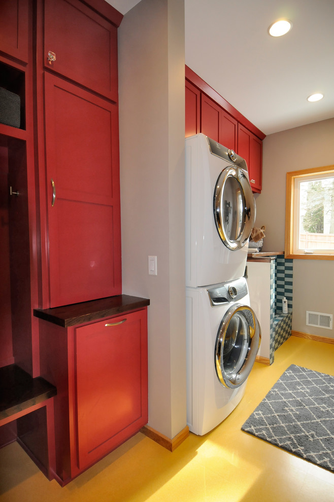 Design ideas for a mid-sized contemporary single-wall utility room in Minneapolis with an undermount sink, shaker cabinets, red cabinets, wood benchtops, beige walls, laminate floors, a stacked washer and dryer and yellow floor.