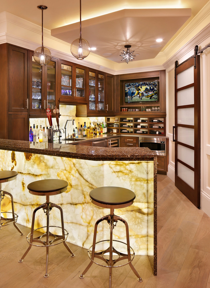 This is an example of a transitional u-shaped seated home bar in San Francisco with medium hardwood floors, shaker cabinets, dark wood cabinets, beige splashback, stone slab splashback and beige floor.