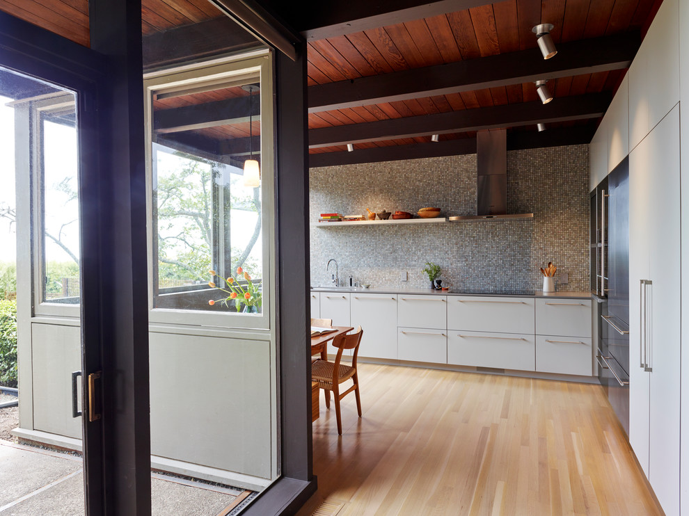 Photo of a large midcentury single-wall eat-in kitchen in San Francisco with an integrated sink, flat-panel cabinets, grey cabinets, grey splashback, glass tile splashback, stainless steel appliances, light hardwood floors, no island, beige floor and grey benchtop.