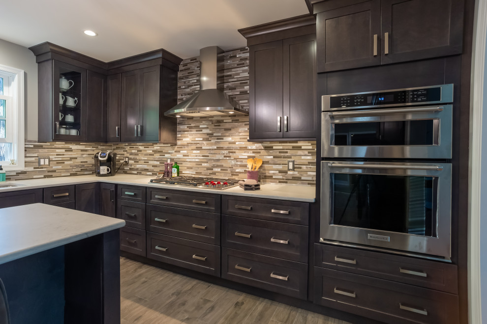 Photo of a large transitional l-shaped eat-in kitchen in Philadelphia with an undermount sink, recessed-panel cabinets, dark wood cabinets, quartz benchtops, multi-coloured splashback, porcelain splashback, stainless steel appliances, medium hardwood floors, with island, brown floor and white benchtop.