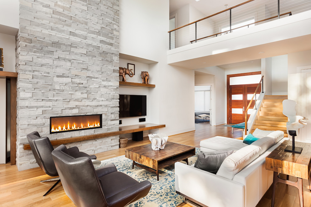 Photo of a contemporary open concept living room in Miami with white walls, light hardwood floors, a ribbon fireplace, a stone fireplace surround, a wall-mounted tv and beige floor.