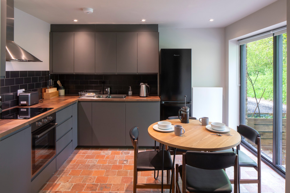 Inspiration for a small contemporary l-shaped eat-in kitchen with an integrated sink, flat-panel cabinets, grey cabinets, wood benchtops, black splashback, ceramic splashback, panelled appliances, terra-cotta floors, no island, red floor and brown benchtop.