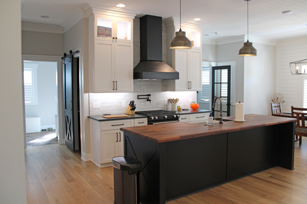 Exempel på ett stort lantligt svart svart kök, med en rustik diskho, skåp i shakerstil, vita skåp, bänkskiva i kvarts, grått stänkskydd, stänkskydd i porslinskakel, svarta vitvaror, ljust trägolv, en köksö och brunt golv