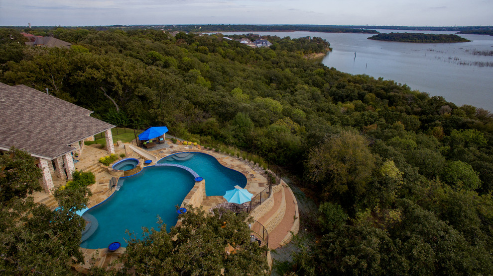 This is an example of a large transitional backyard custom-shaped infinity pool in Dallas with a water slide and natural stone pavers.