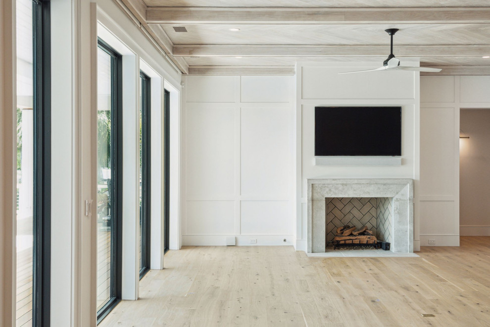 На фото: открытая гостиная комната в морском стиле с белыми стенами, светлым паркетным полом, стандартным камином, фасадом камина из бетона, телевизором на стене и деревянным потолком