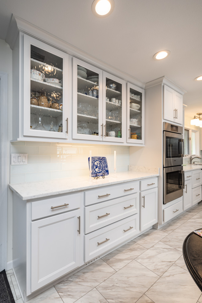 Enclosed kitchen - large transitional l-shaped ceramic tile and white floor enclosed kitchen idea with an undermount sink, shaker cabinets, white cabinets, quartz countertops, white backsplash, subway tile backsplash, stainless steel appliances, an island and white countertops