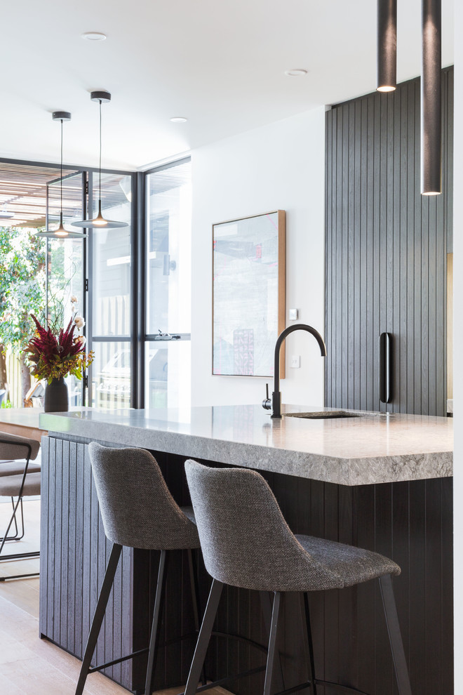 Inspiration for a mid-sized contemporary galley open plan kitchen in Melbourne with black cabinets, quartz benchtops, light hardwood floors, with island, grey benchtop, an undermount sink, flat-panel cabinets and beige floor.