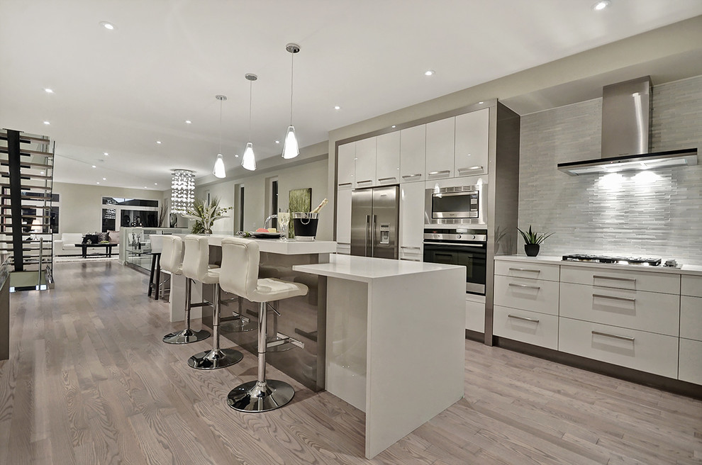 Inspiration for a mid-sized contemporary single-wall open plan kitchen in Ottawa with an undermount sink, flat-panel cabinets, white cabinets, solid surface benchtops, grey splashback, matchstick tile splashback, stainless steel appliances, laminate floors, with island, brown floor and white benchtop.